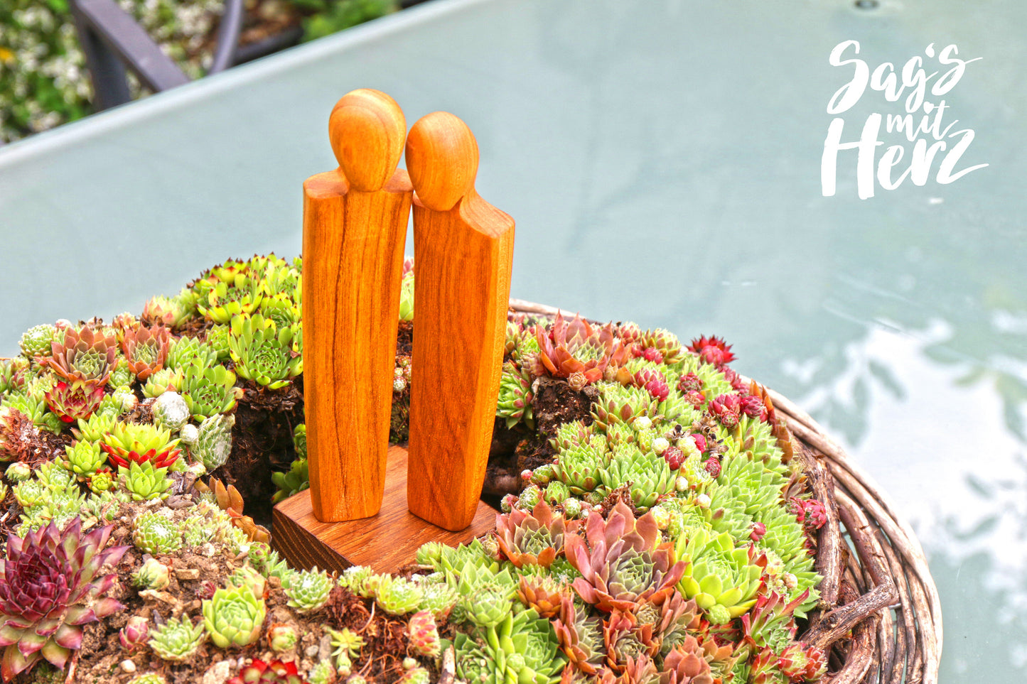 Zierholz-Figur 'Ohne Worte' von Thankgoods im Pflanzenkranz auf Glastisch, 23,5 cm hoch, perfekte Coaching-Deko für Outdoor-Bereiche.